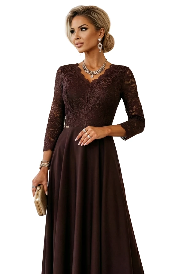 Modelka prezentuje długą czekoladową sukienkę maxi z koronkową górą, rękawem 3/4 i seksownym rozcięciem – idealna kreacja na specjalne okazje.