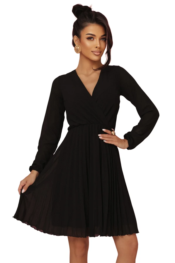 Modelka prezentuje elegancką czarną szyfonową sukienkę marki Numoco z długim rękawem, kopertowym dekoltem i plisowanym dołem – idealną na wieczór, wesele lub specjalne okazje. Produkt polski, sfotografowany na różowym tle.