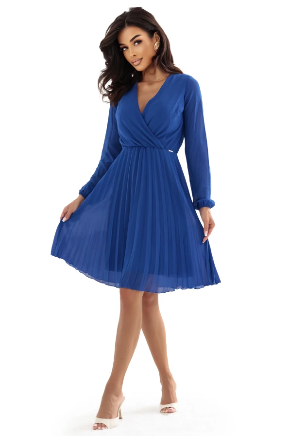 Modelka prezentuje elegancką chabrową sukienkę z kopertowym dekoltem i plisowanym dołem. Stylizacja marki Numoco została sfotografowana w jasnym, nowoczesnym wnętrzu, co podkreśla lekkość i szyk kreacji.