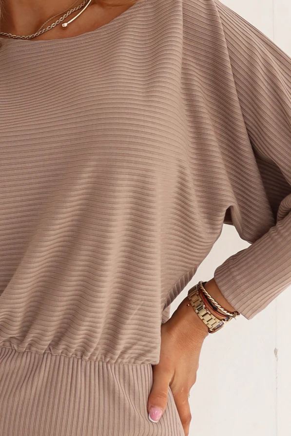 Beżowa sukienka ołówkowa mocha mousse z prążkowanego materiału prezentowana przez modelkę w jasnym, nowoczesnym wnętrzu.