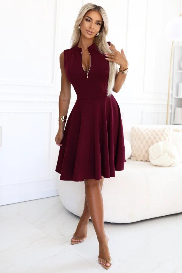 Modelka prezentuje elegancką bordową sukienkę bez rękawów z ozdobnym zamkiem i rozkloszowanym dołem, idealną na wyjątkowe okazje.