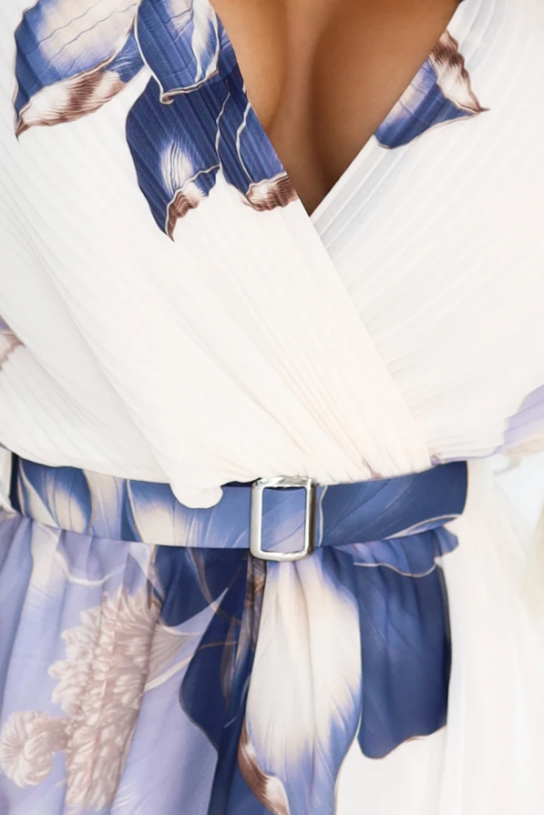 Modelka z uśmiechem prezentuje lekką, szyfonową sukienkę midi z kwiatowym wzorem w odcieniach niebieskiego. Stylizacja emanuje kobiecą delikatnością i letnim wdziękiem, idealna na wyjątkowe okazje i codzienne chwile.