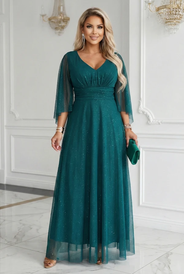 Modelka w szmaragdowej wieczorowej sukience plus size maxi z brokatowym połyskiem i rękawami typu motyl w jasnym wnętrzu - dla puszystych.